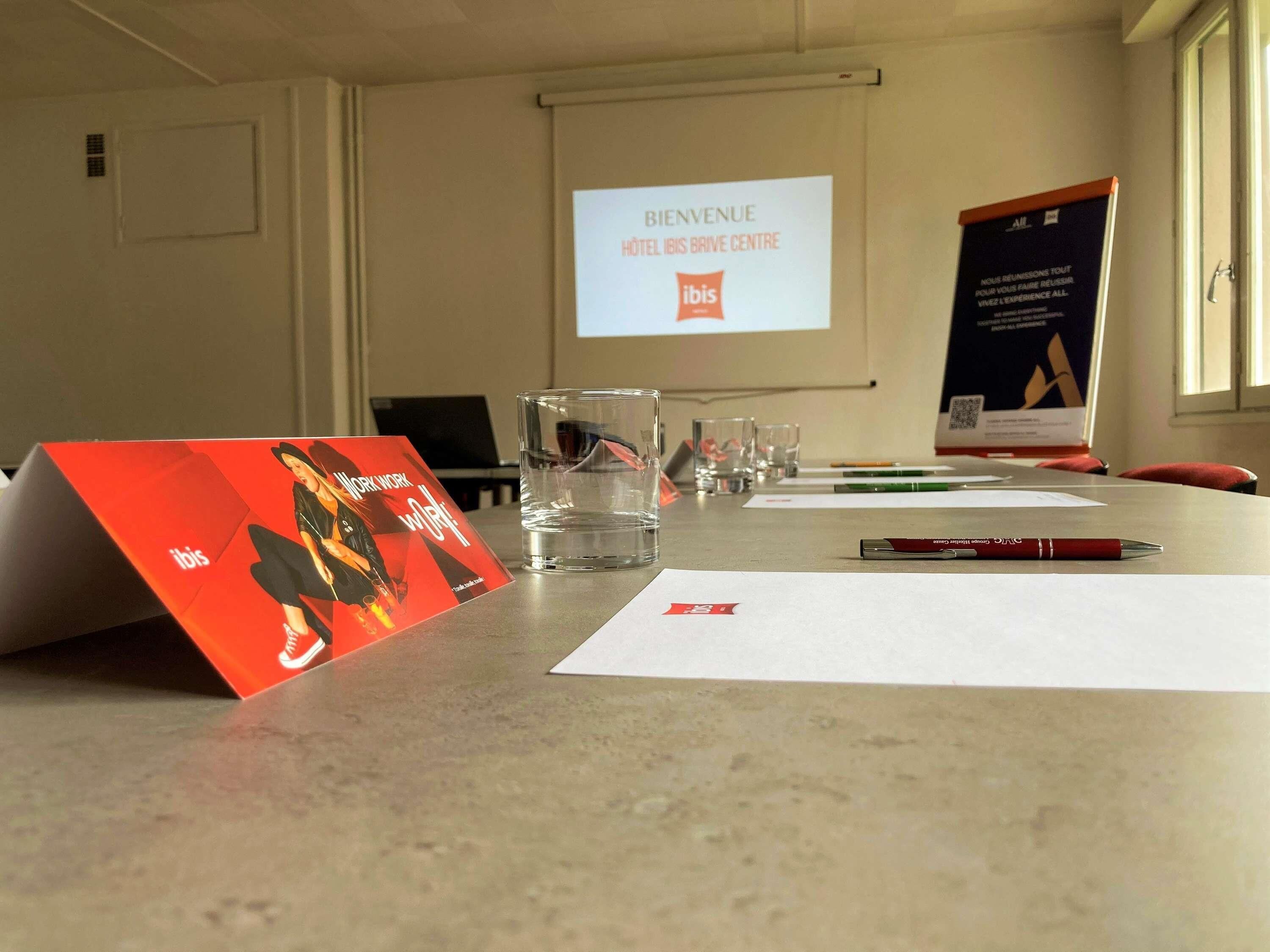 A conference room with a projector screen displaying 'BIENVENUE HOTEL BRIVE CENTRE' and a welcome message.