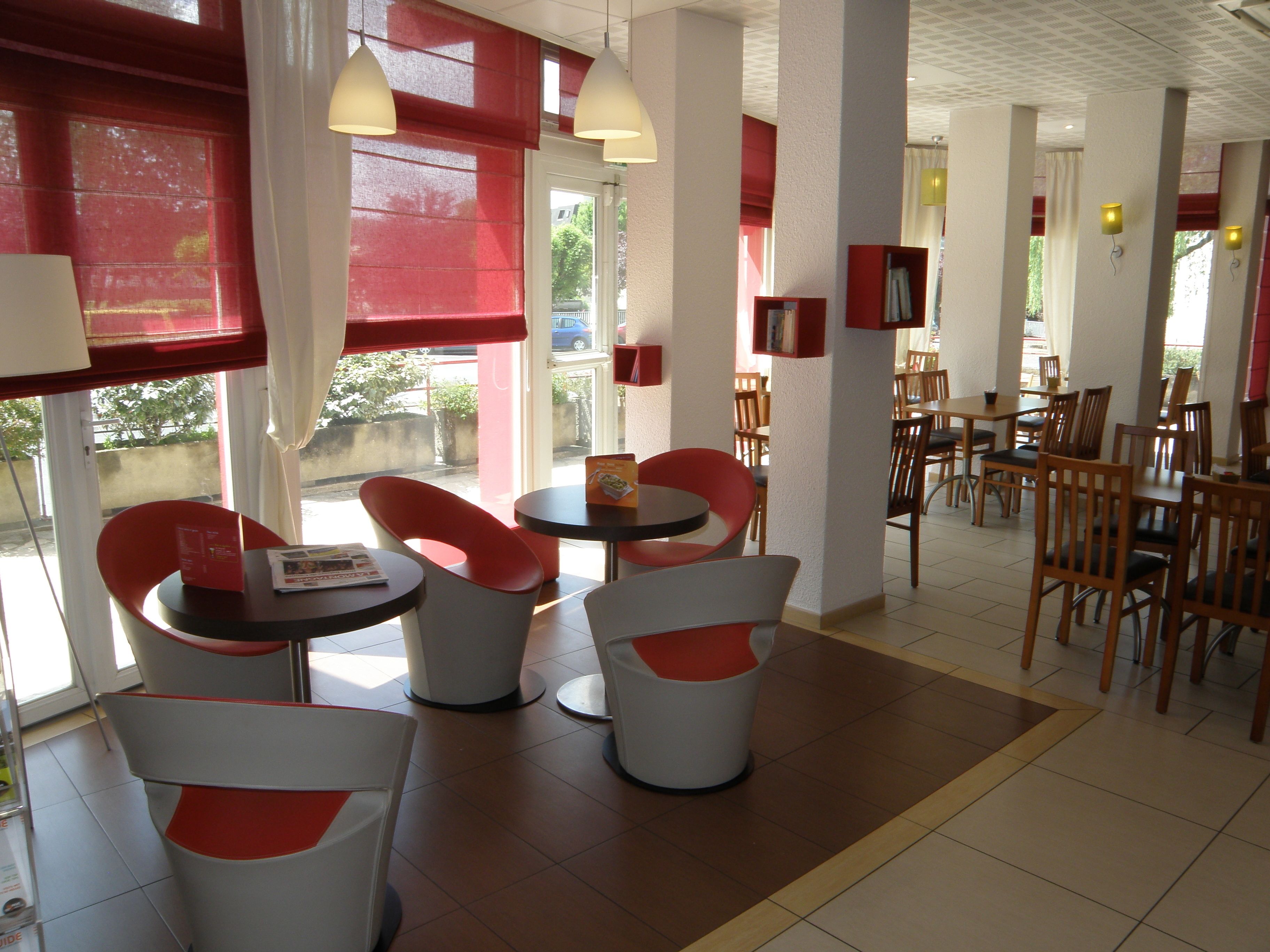 Un restaurante con sillas rojas y blancas, mesas redondas e iluminación colgante.