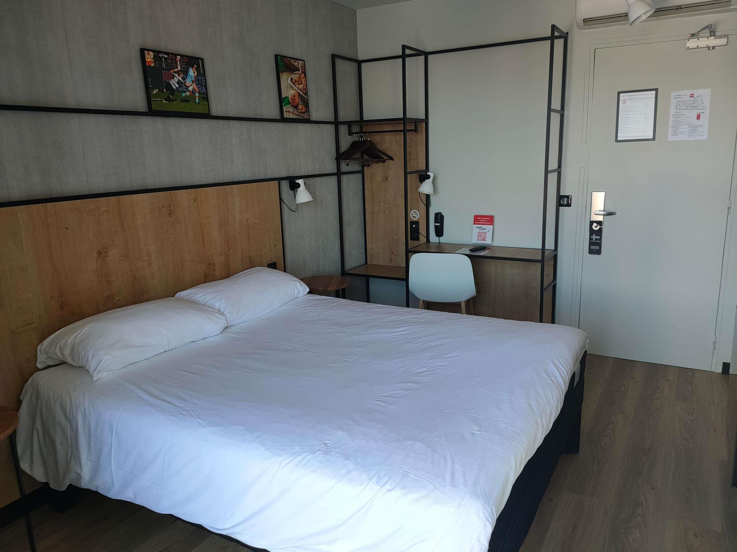 Habitación de hotel con cama, escritorio, silla, lámpara y puerta con un cartel.