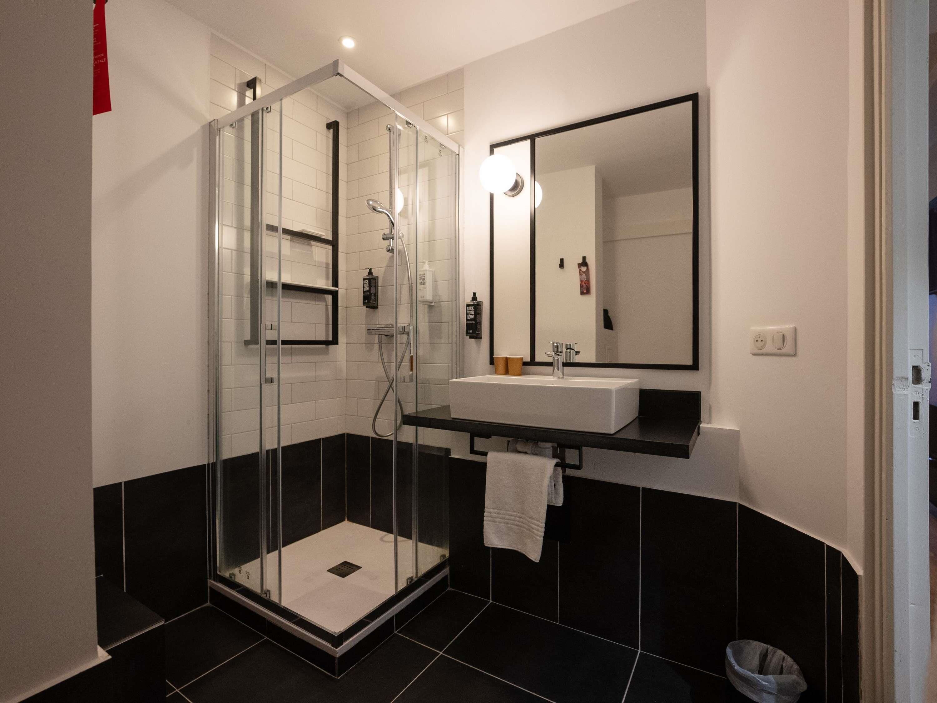 A modern bathroom with a glass-enclosed shower, a white sink, and a large mirror.