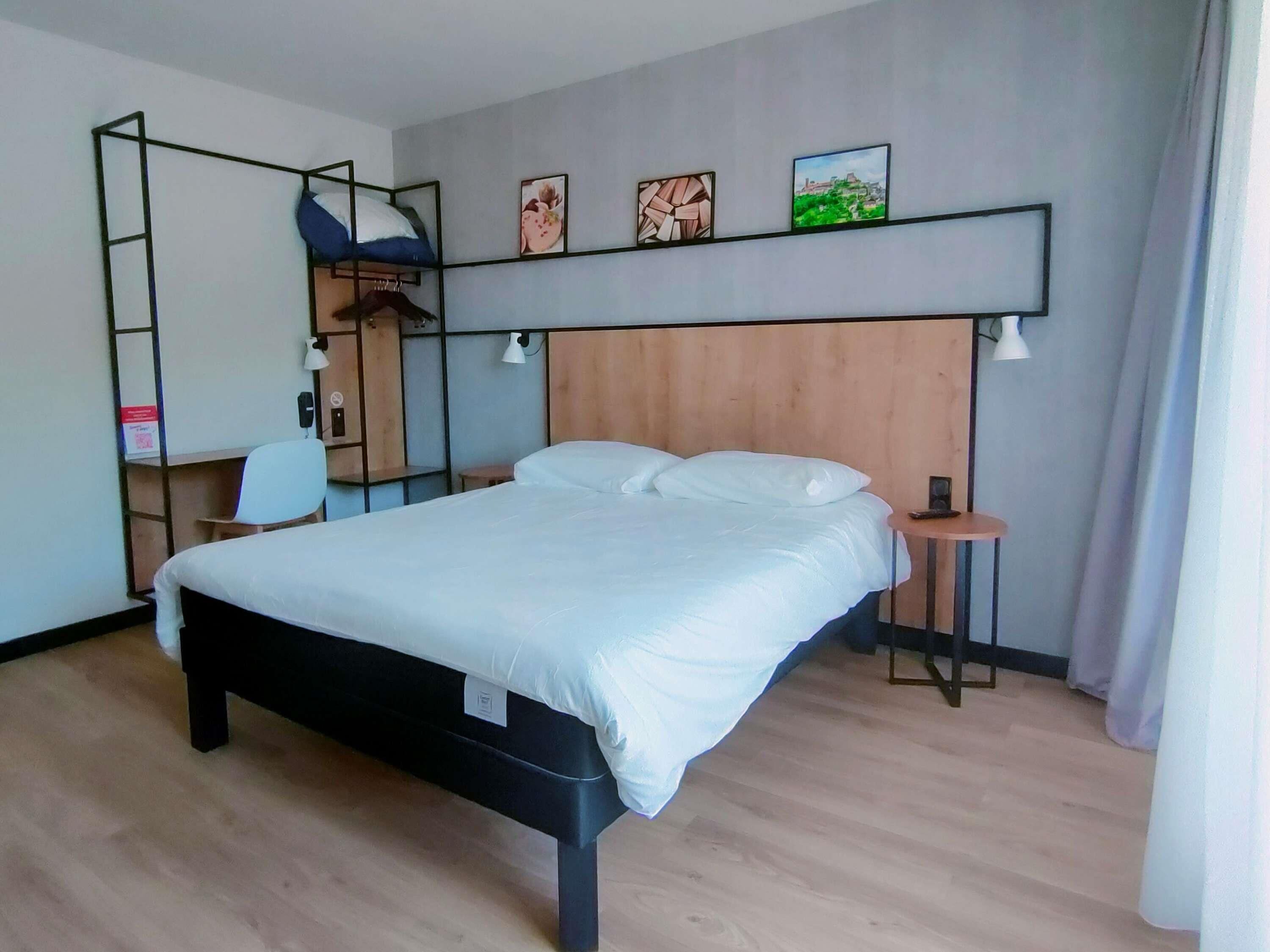 A modern hotel room with a large bed, a desk, a chair, and a wardrobe.