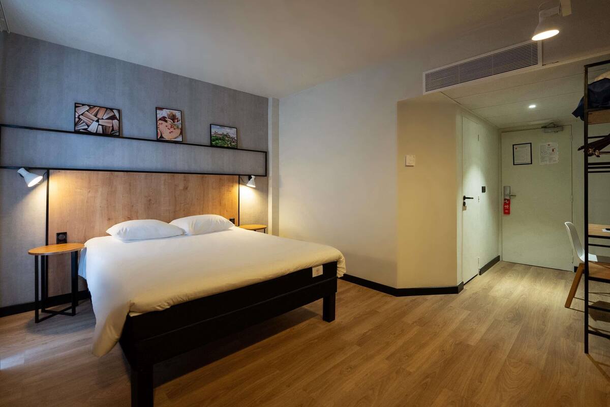 A bedroom with a bed, bedside tables, a wall-mounted shelf with pictures, and a door leading to another room.