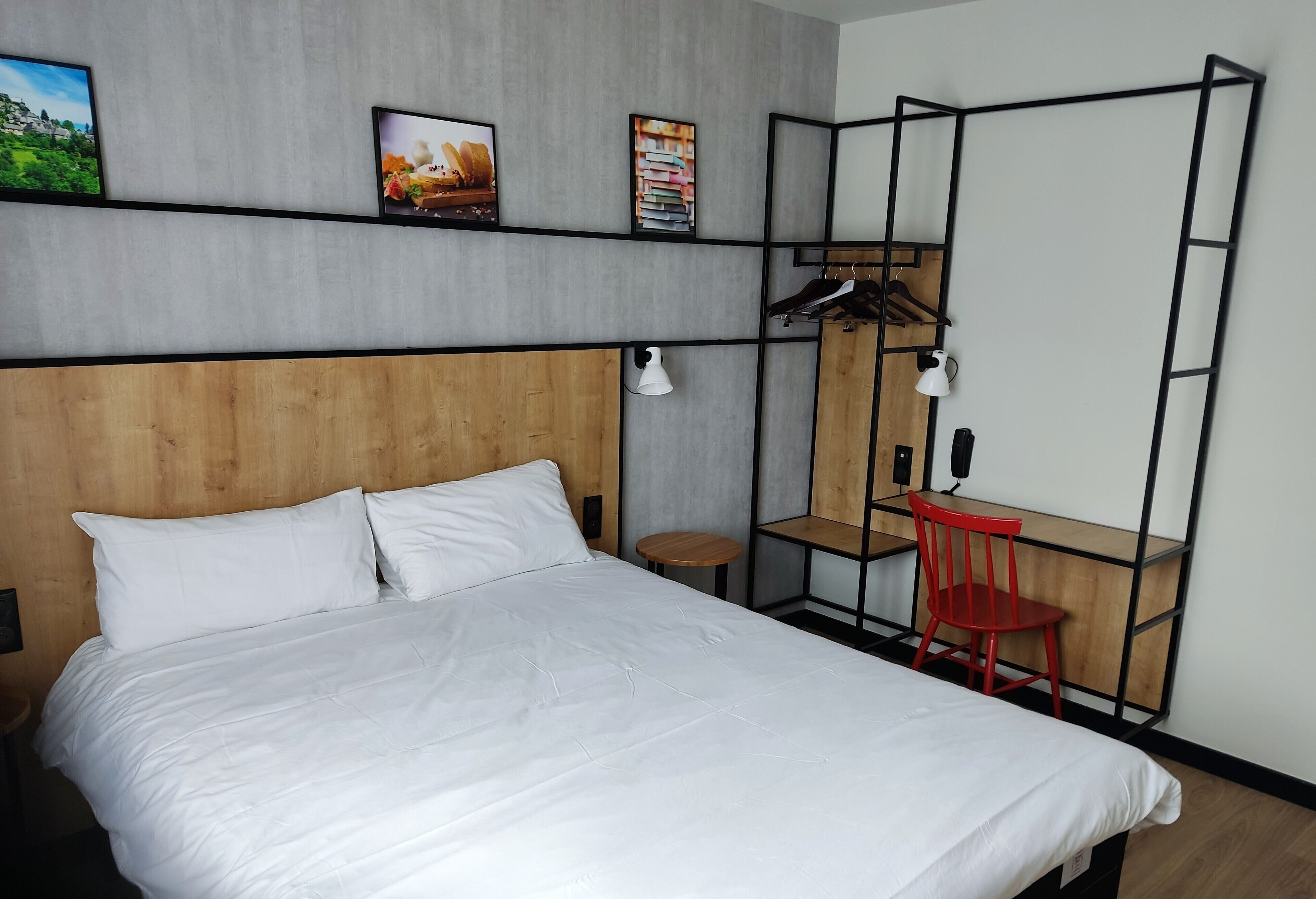 A bedroom with a bed, a desk, a chair, a hanging coat rack, and a small round table.