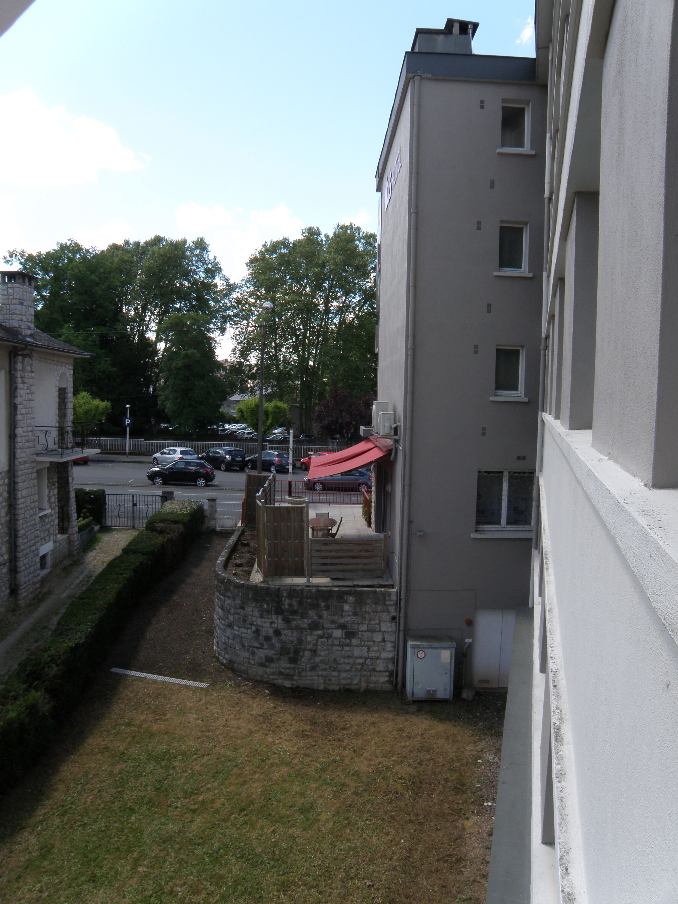 A courtyard with a stone wall, a red umbrella, and a view of a street with parked cars.