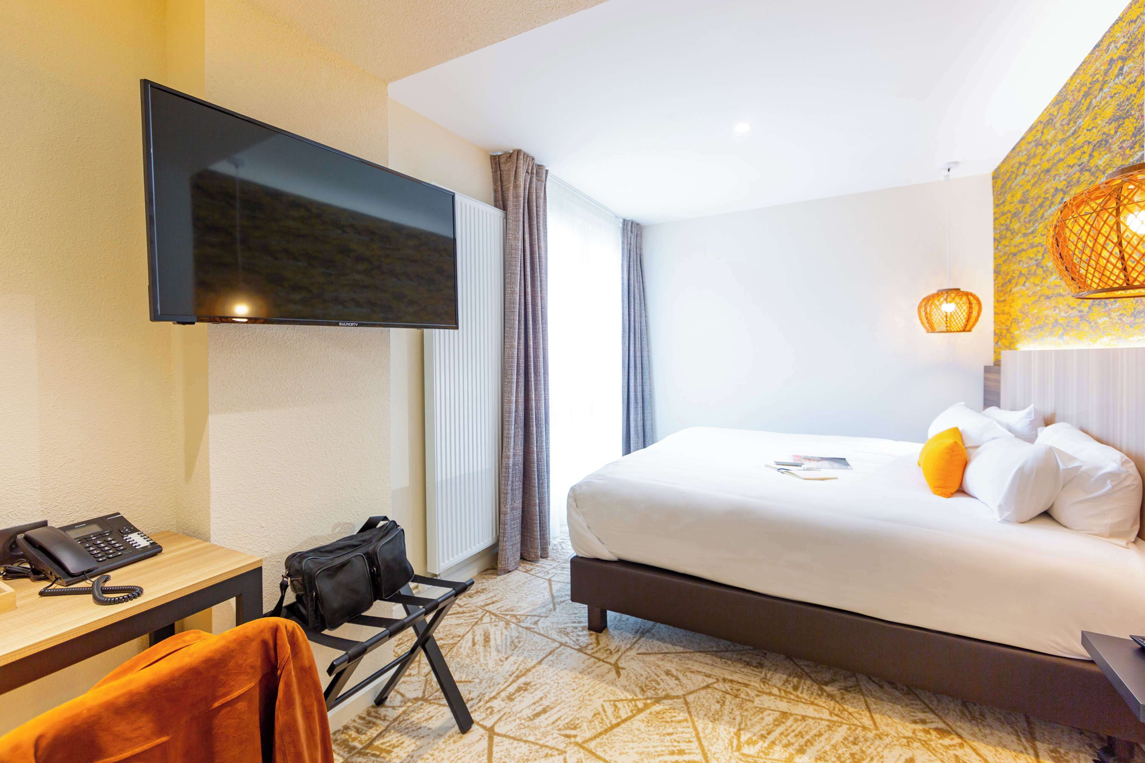 Habitación de hotel con cama, escritorio con teléfono, una silla y televisión montada en la pared.