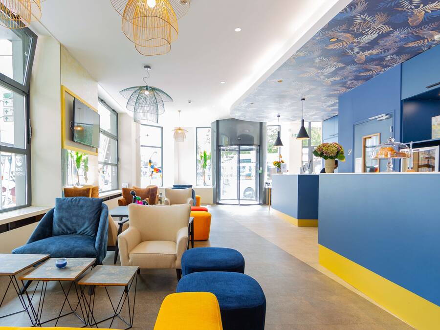 A modern hotel lobby with seating areas, a reception desk, and decorative ceiling lights.