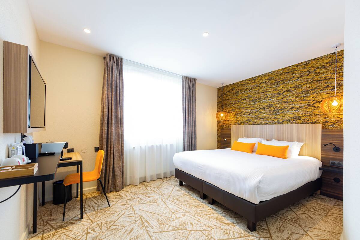 Habitación de hotel con una cama, un escritorio con silla, una computadora y una lámpara.