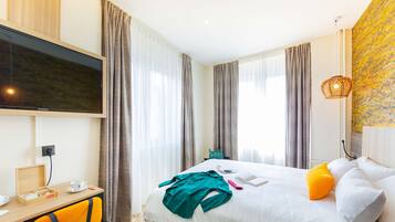 A hotel room with a bed, a desk with a television, a chair, and a window with curtains.