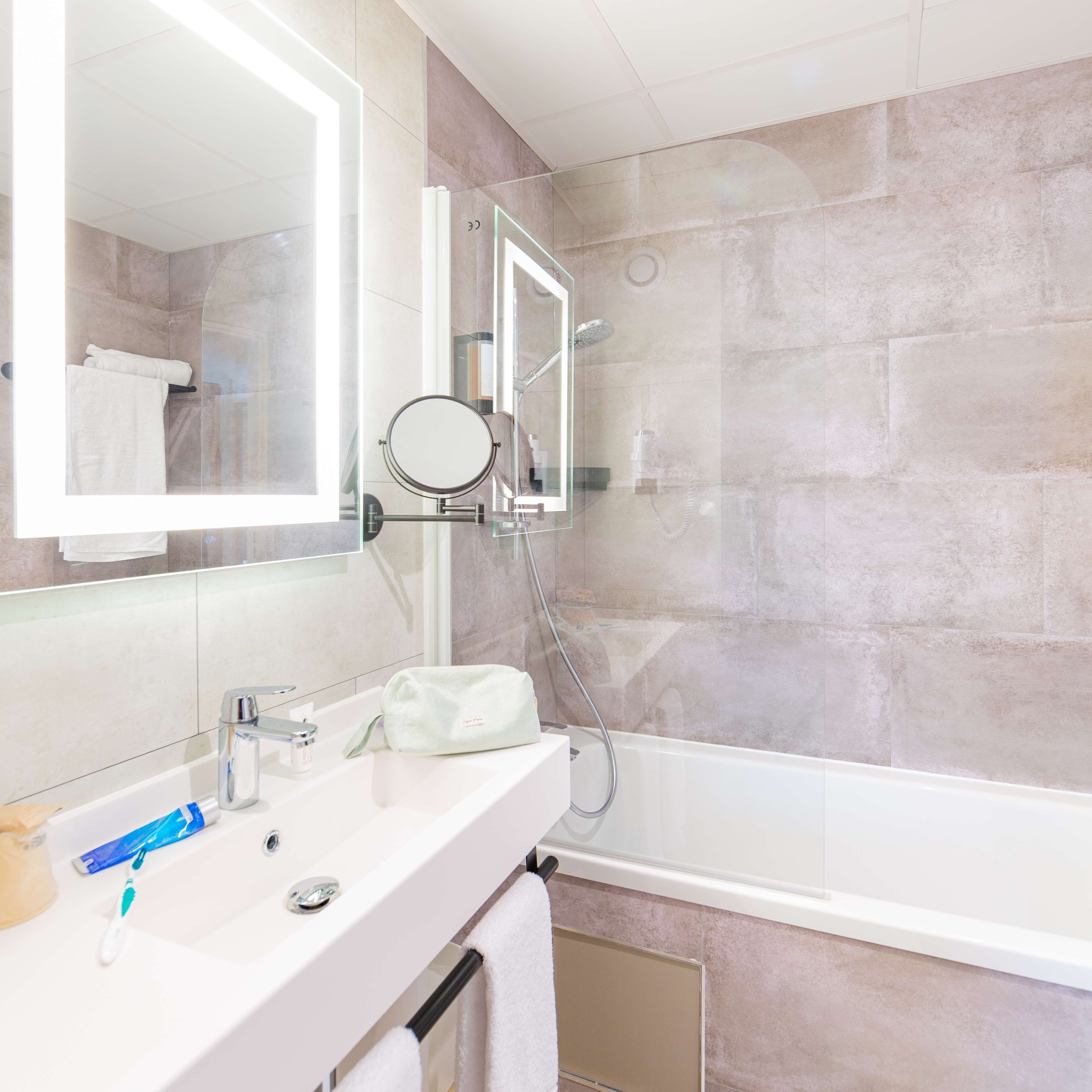 A modern bathroom with a large mirror, a sink with toiletries, a handheld showerhead, and a bathtub.