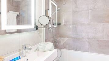 A modern bathroom with a large mirror, a sink with toiletries, a handheld showerhead, and a bathtub.