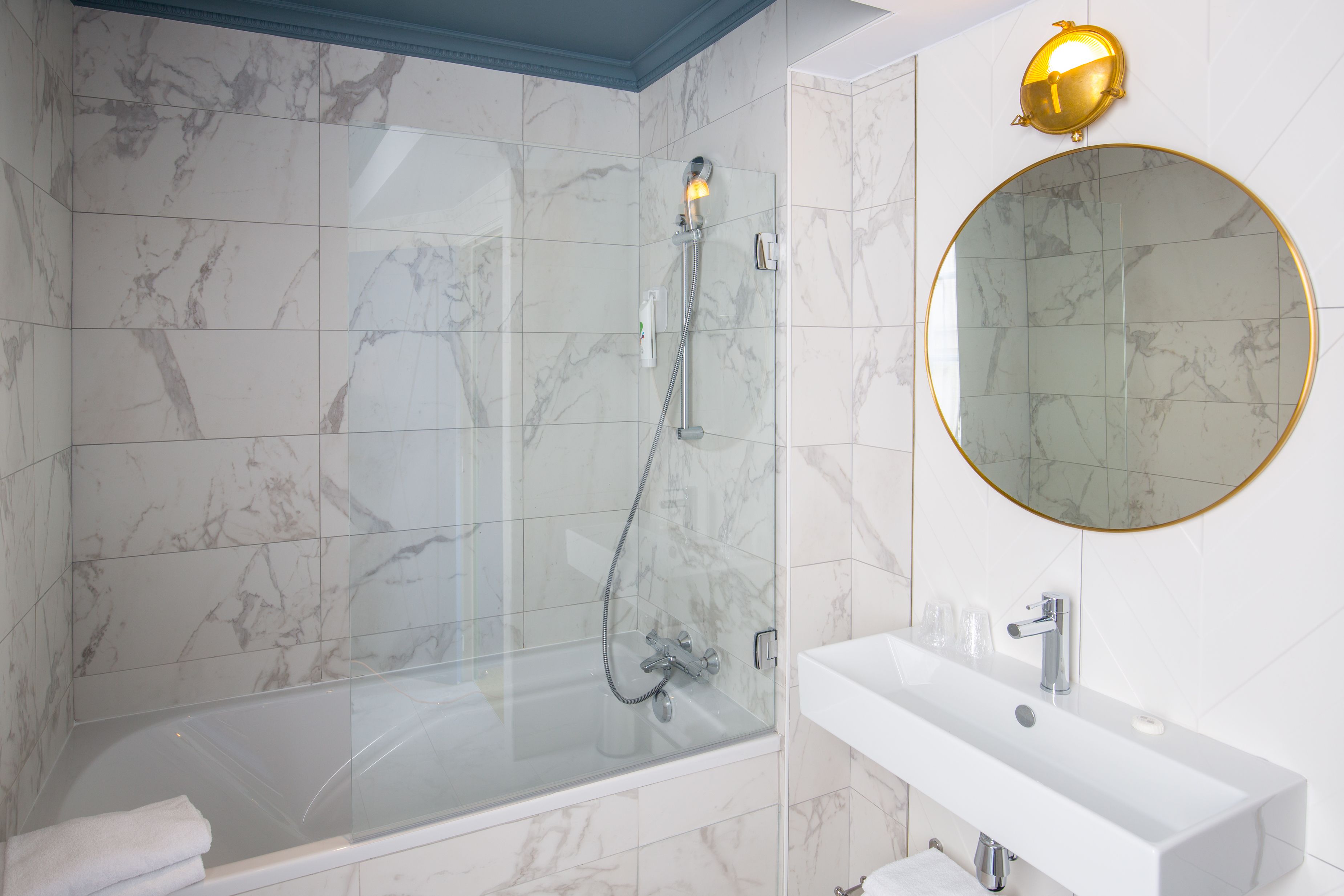 Une salle de bain moderne avec une douche à parois de verre, un lavabo blanc et un miroir rond doté d’un cadre doré.