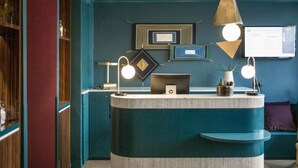 A reception desk with a computer, framed pictures on the wall, and a blue wall. - ibis Styles Paris Nation Cours de Vincennes (Paris)