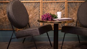 A room with a woven wall panel, two black chairs, a round table with a white cup and a purple flower arrangement. - ibis Styles Paris Nation Cours de Vincennes (Paris)