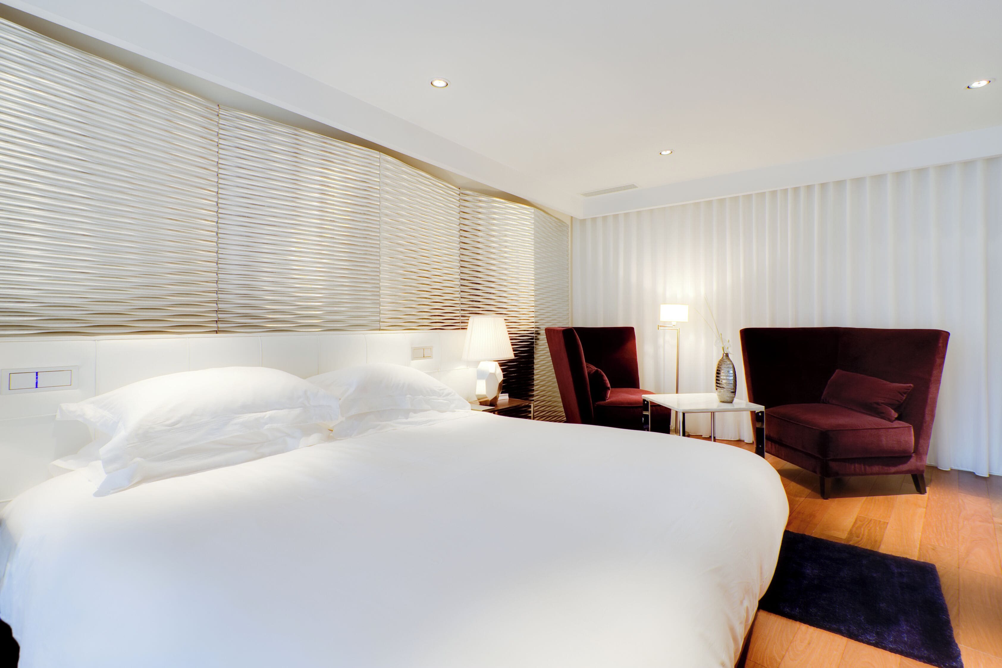 A hotel room with a large bed, two chairs, a small table, and a lamp.