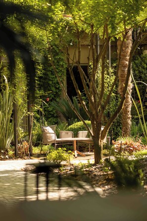 A garden with a bench and a table, surrounded by various plants and trees. - Maison Pic (Valence)