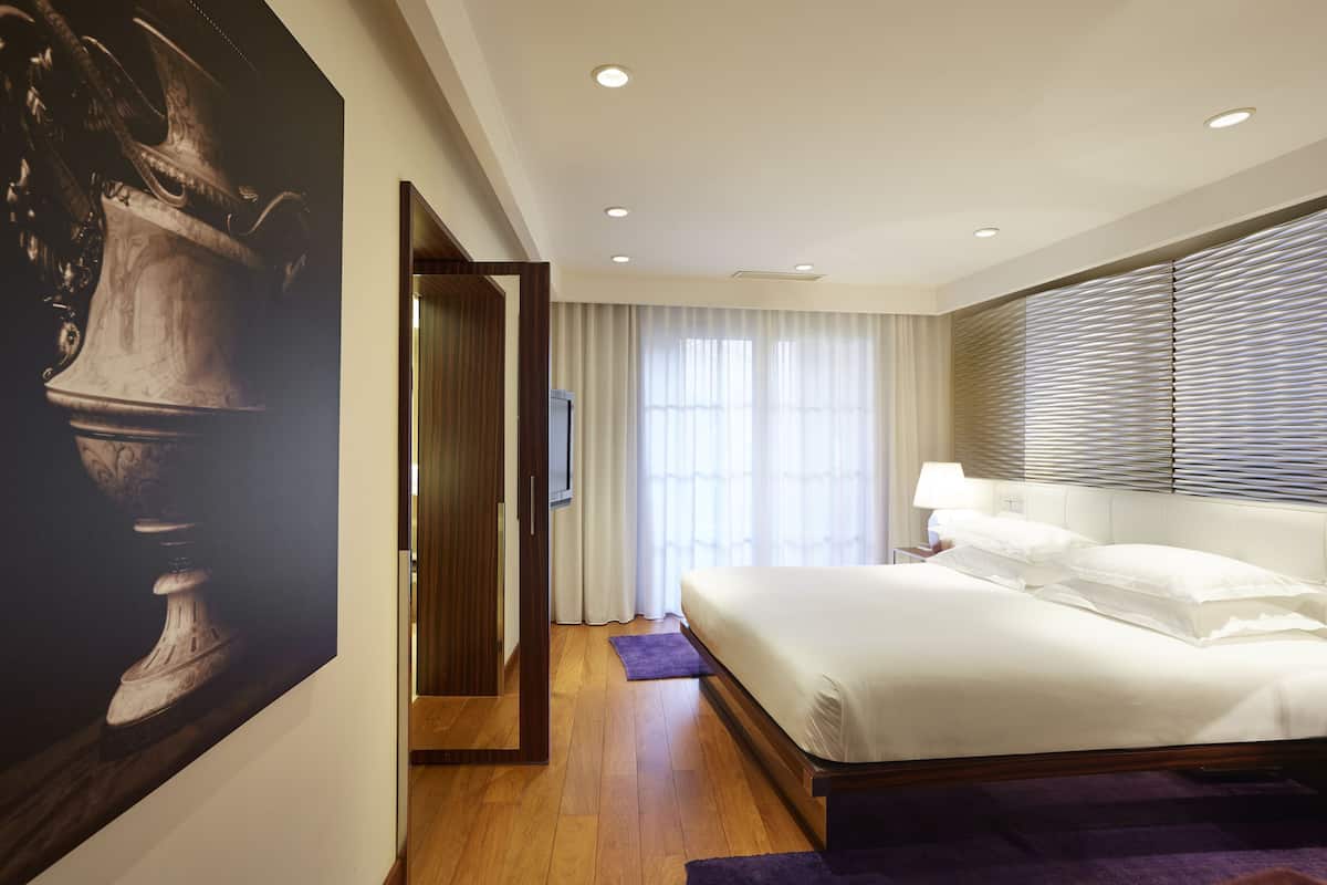 Een moderne hotelkamer met een groot bed, een flatscreen televisie, een houten vloer en een groot schilderij aan de muur.