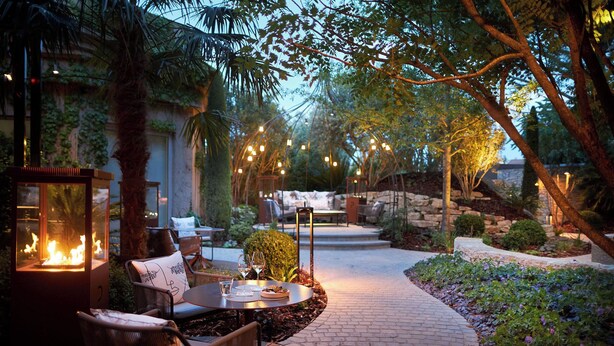 Un patio al aire libre con una chimenea, asientos e iluminación ambiental.