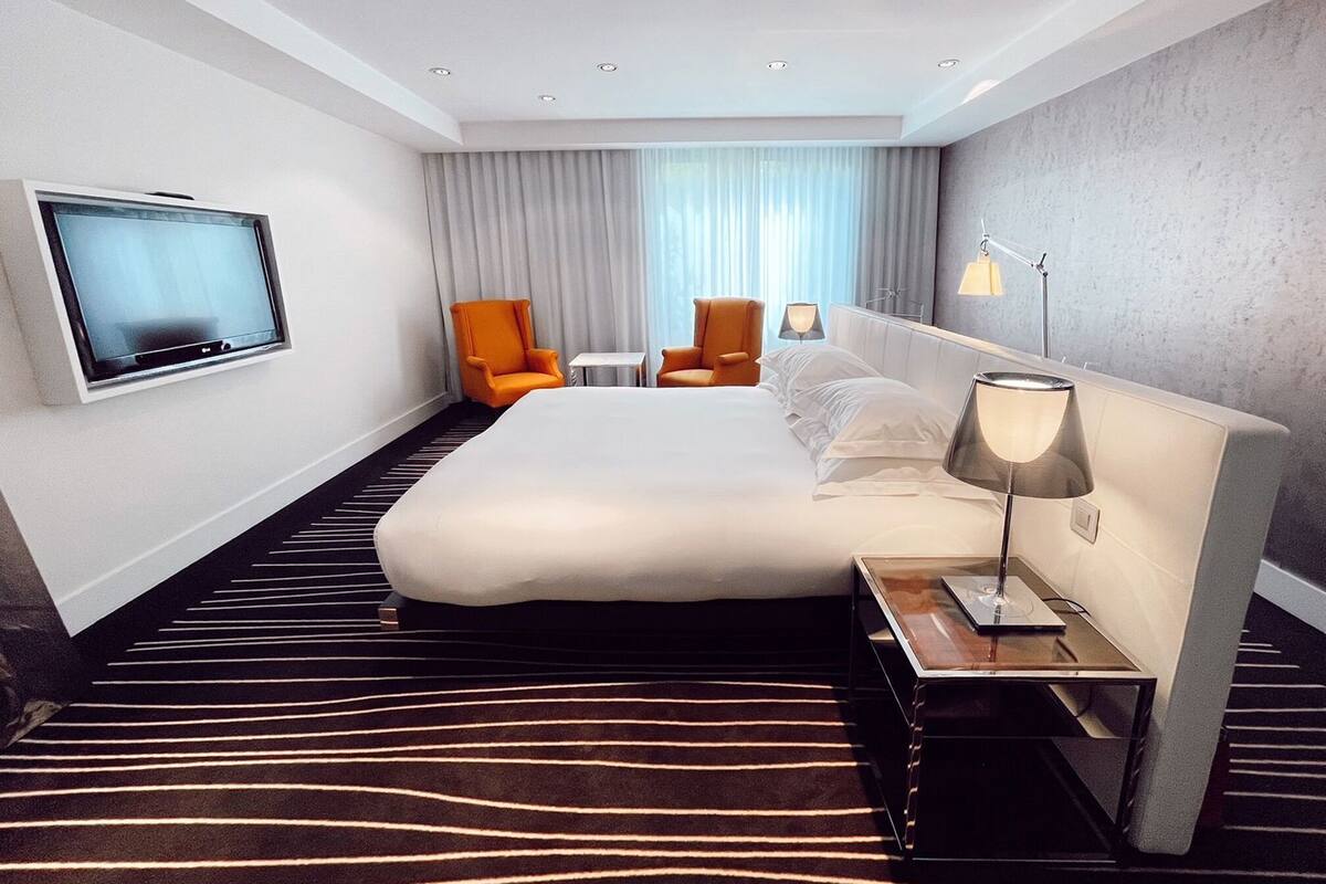 Een moderne hotelkamer met een groot bed, twee oranje fauteuils, een televisie, een bedlampje en een tapijt met zebraprint.