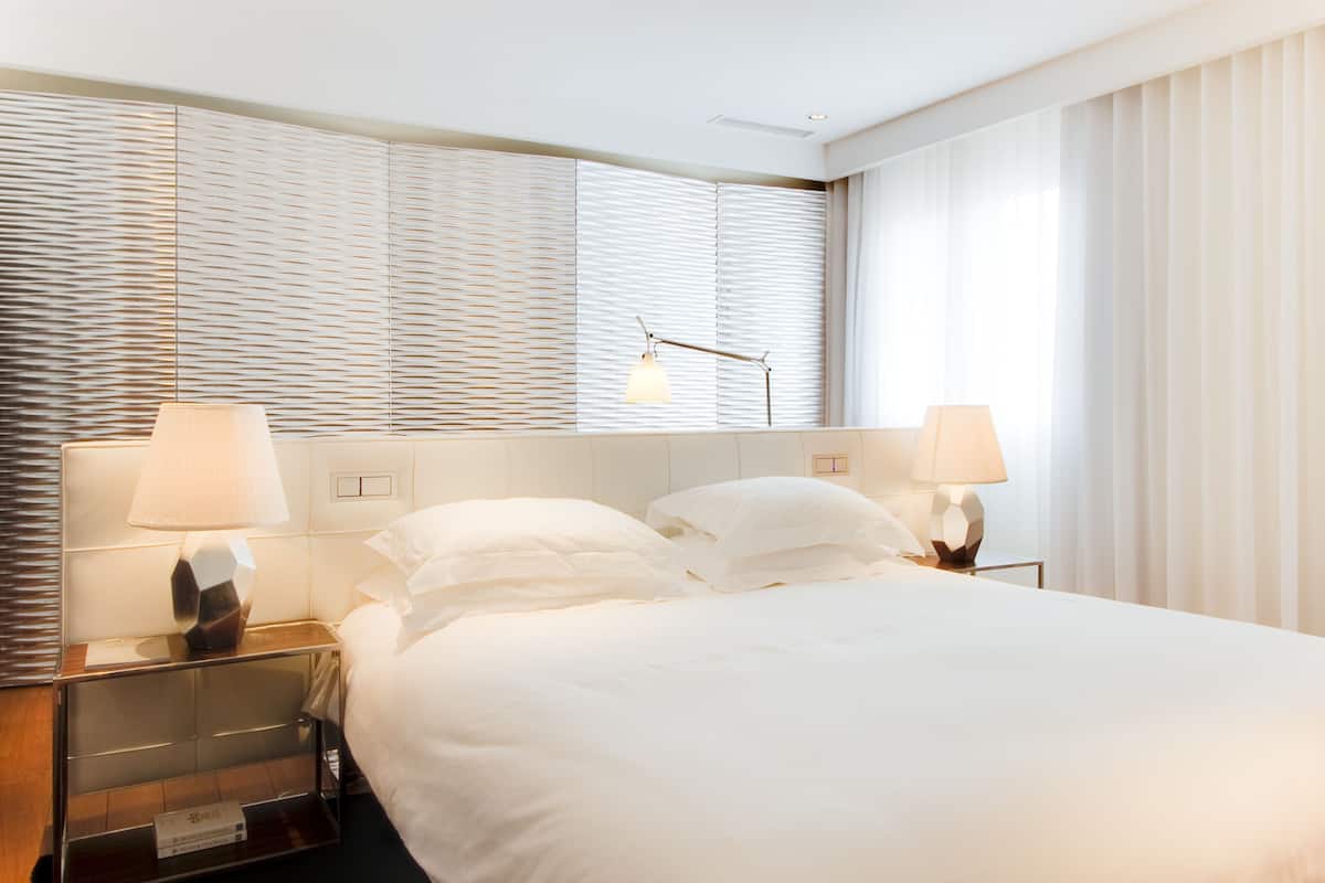 Een hotelkamer met een groot bed, twee bedlampen, een nachtkastje en een raam met jaloezieën.