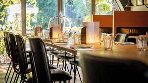 Un restaurante con una larga mesa dispuesta para comer, rodeada de sillas y grandes ventanales con vistas a zonas verdes.