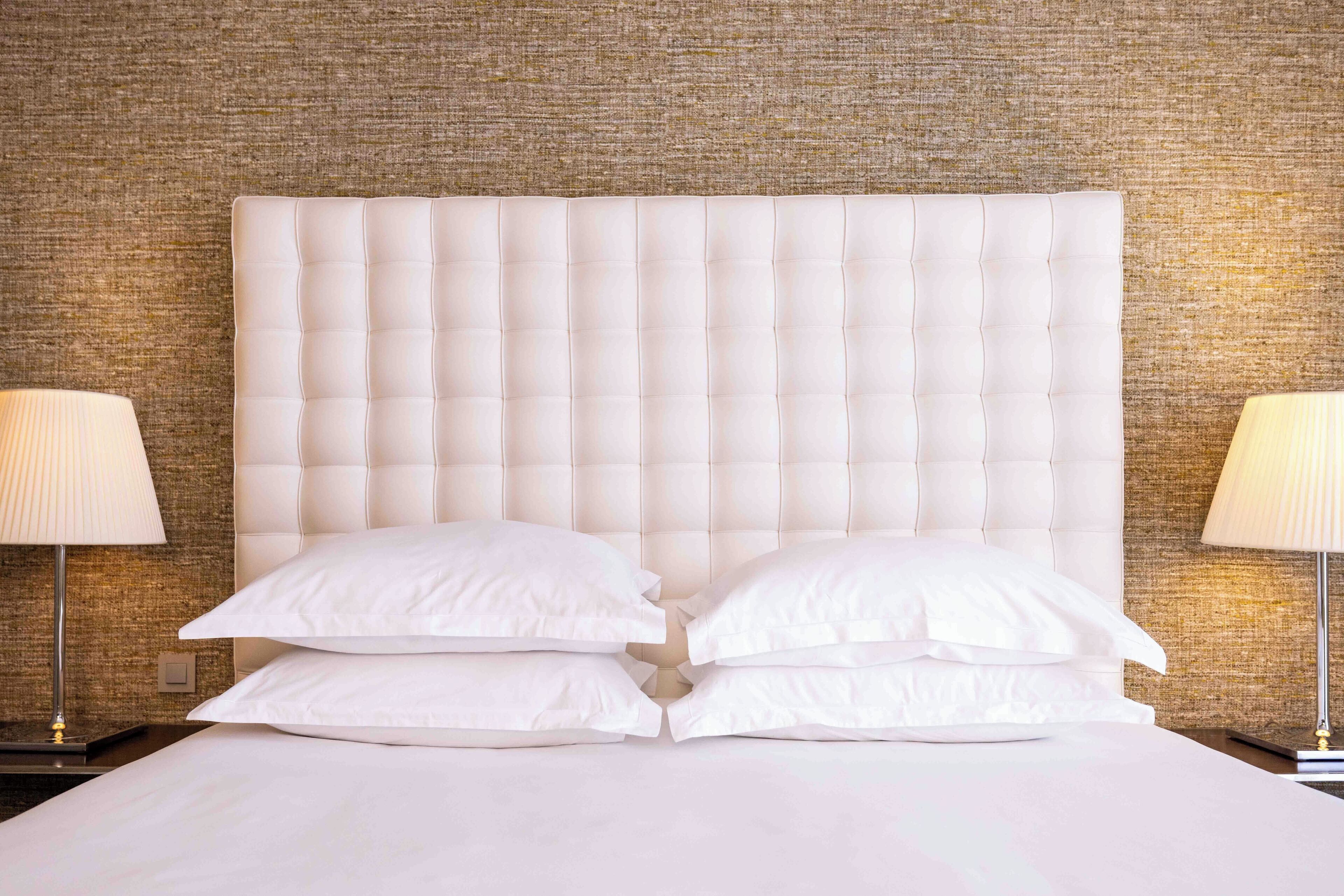A neatly made bed with a tufted headboard, two bedside lamps, and a textured wall behind.