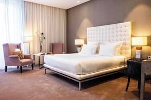 A modern hotel room with a large bed, two armchairs, a small table, and a lamp. - Maison Pic (Valence)