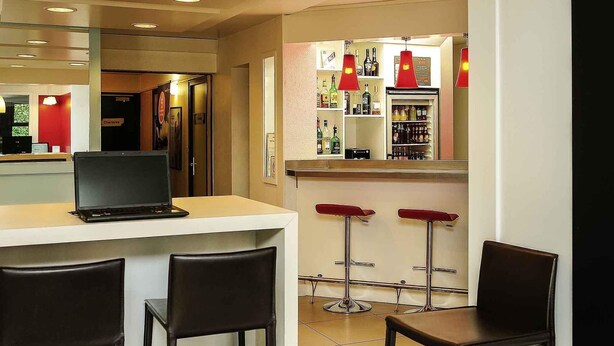 A bar area with a laptop on a counter, two bar stools, and a refrigerator stocked with bottles. - ibis Lyon Est Beynost A42 (Beynost)