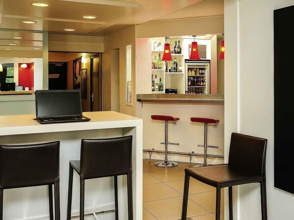 A bar area with a laptop on a counter, two bar stools, and a refrigerator stocked with bottles. - ibis Lyon Est Beynost A42 (Beynost)