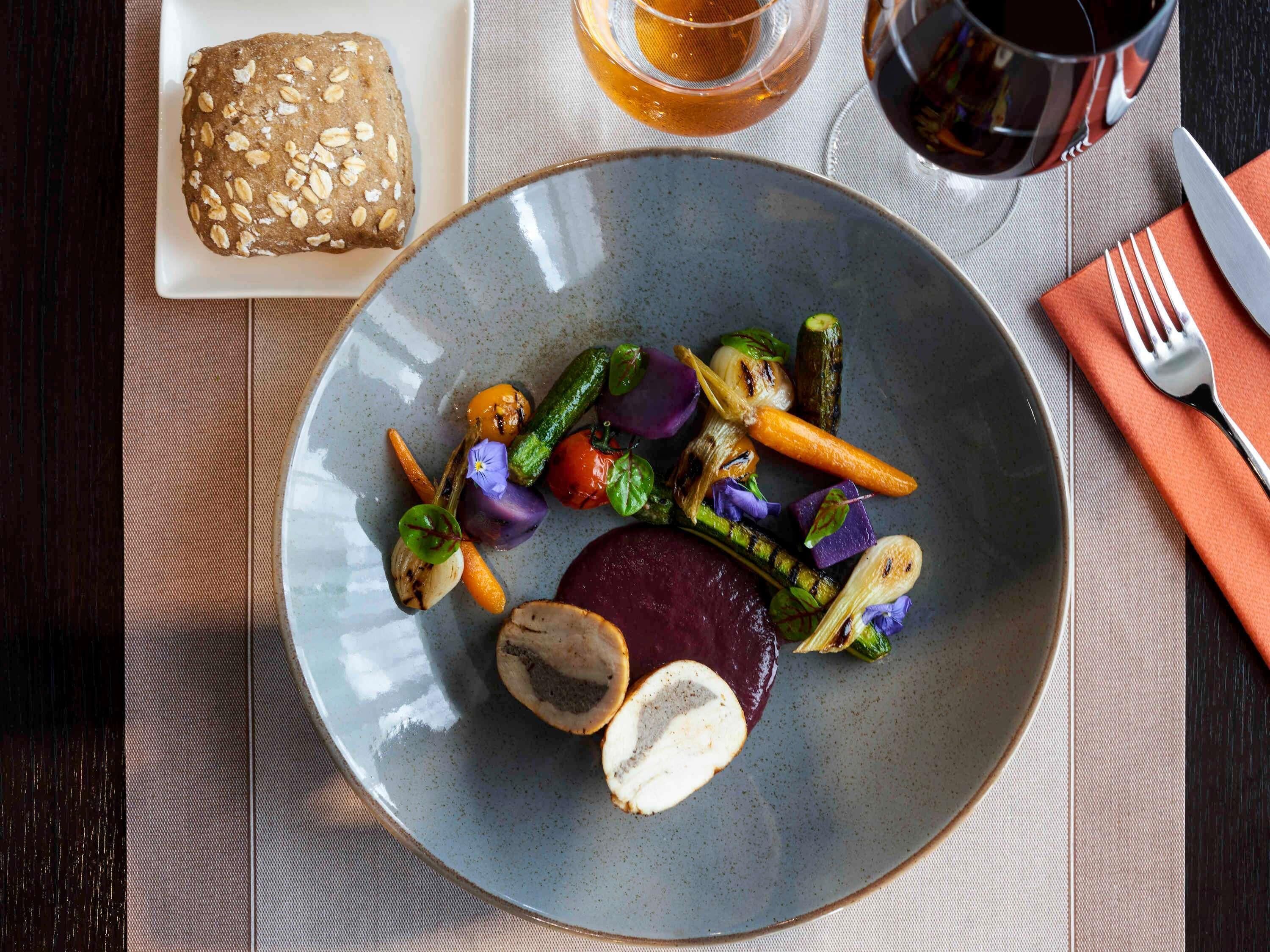 A plate with grilled vegetables and a piece of meat, a loaf of bread, and a glass of tea on a table.