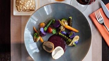 A plate with grilled vegetables and a piece of meat, a loaf of bread, and a glass of tea on a table.