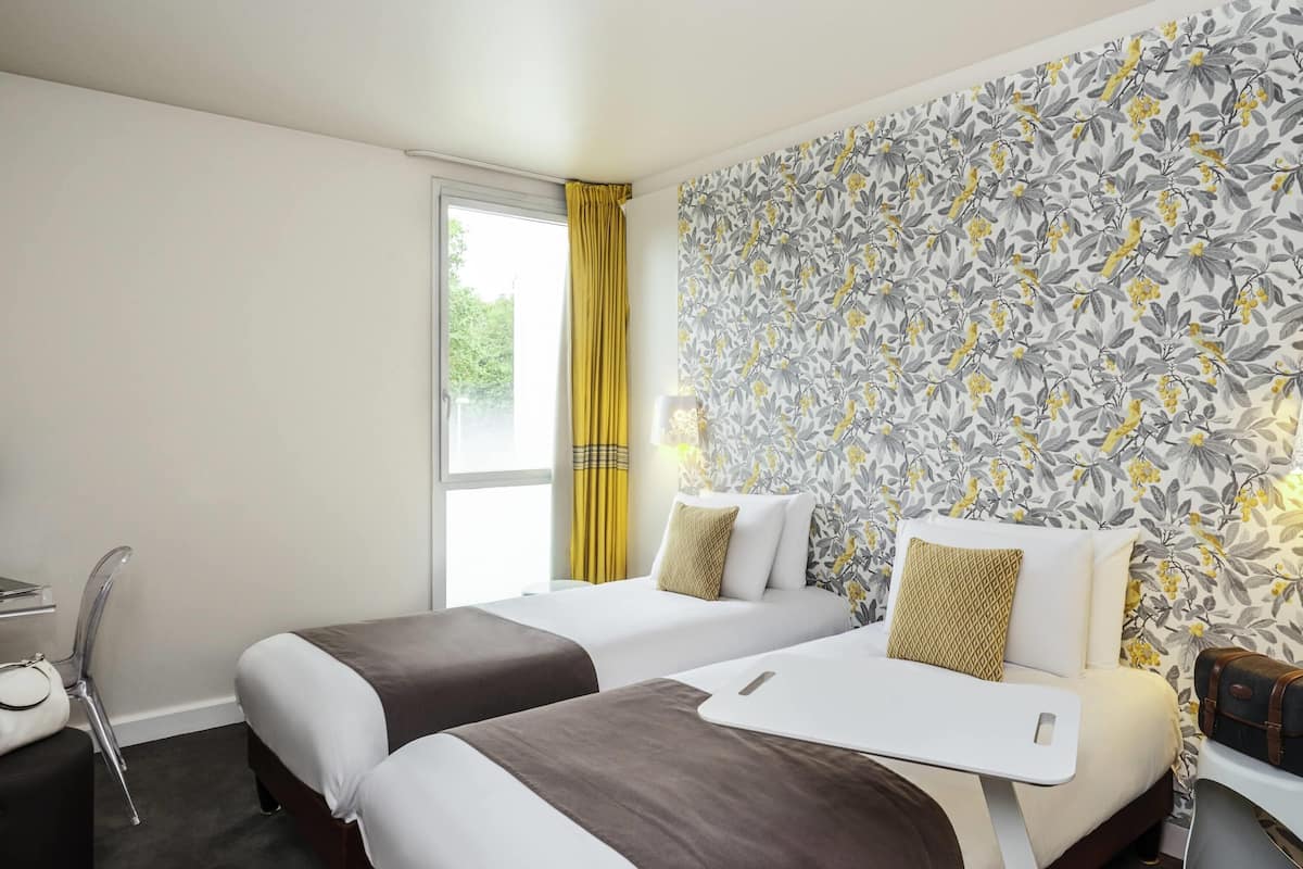Une chambre d’hôtel avec deux lits, un bureau, une chaise et une fenêtre avec des rideaux.