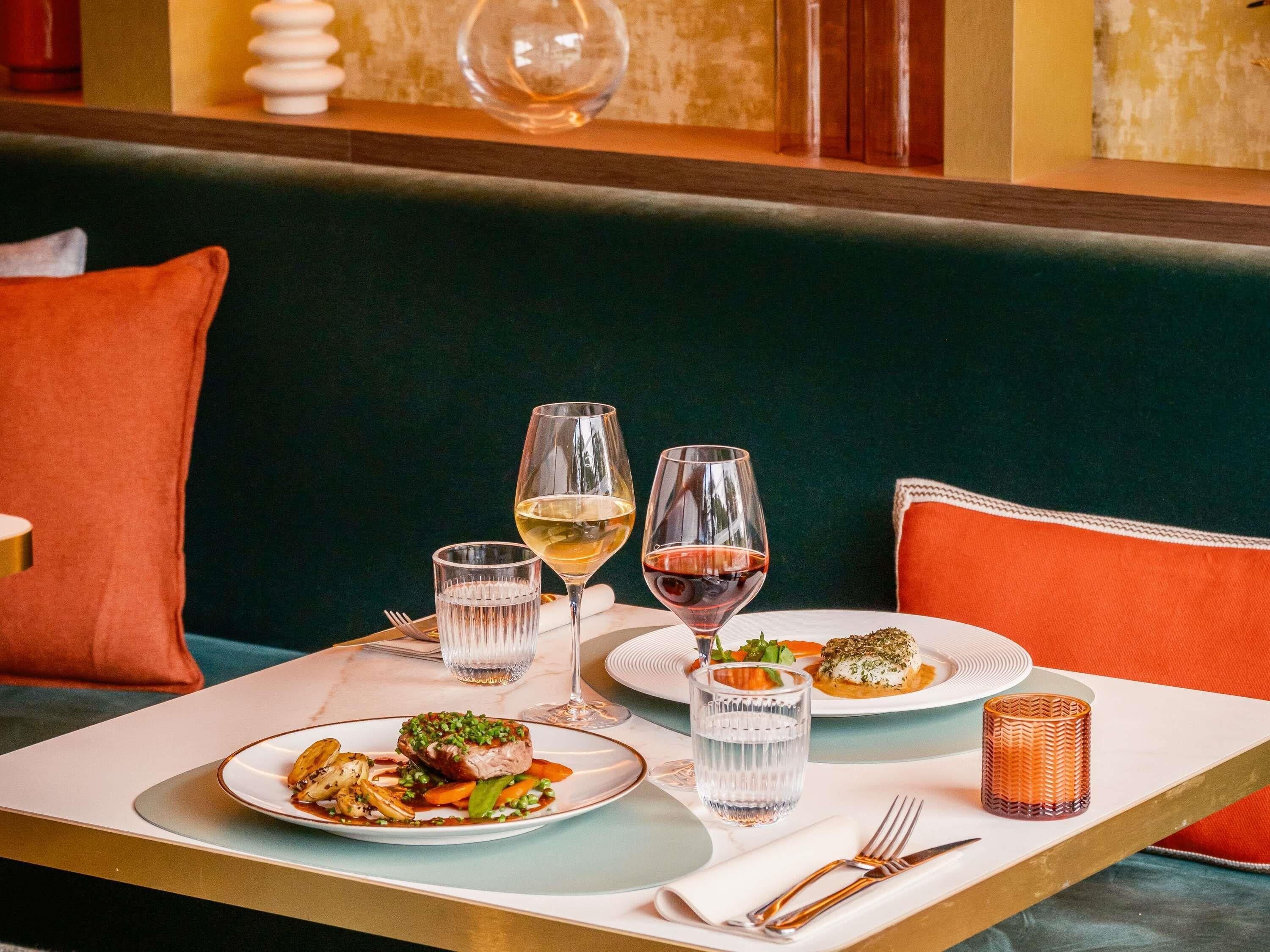 Una mesa de comedor con platos de comida, vasos de agua y vino, y cubiertos.
