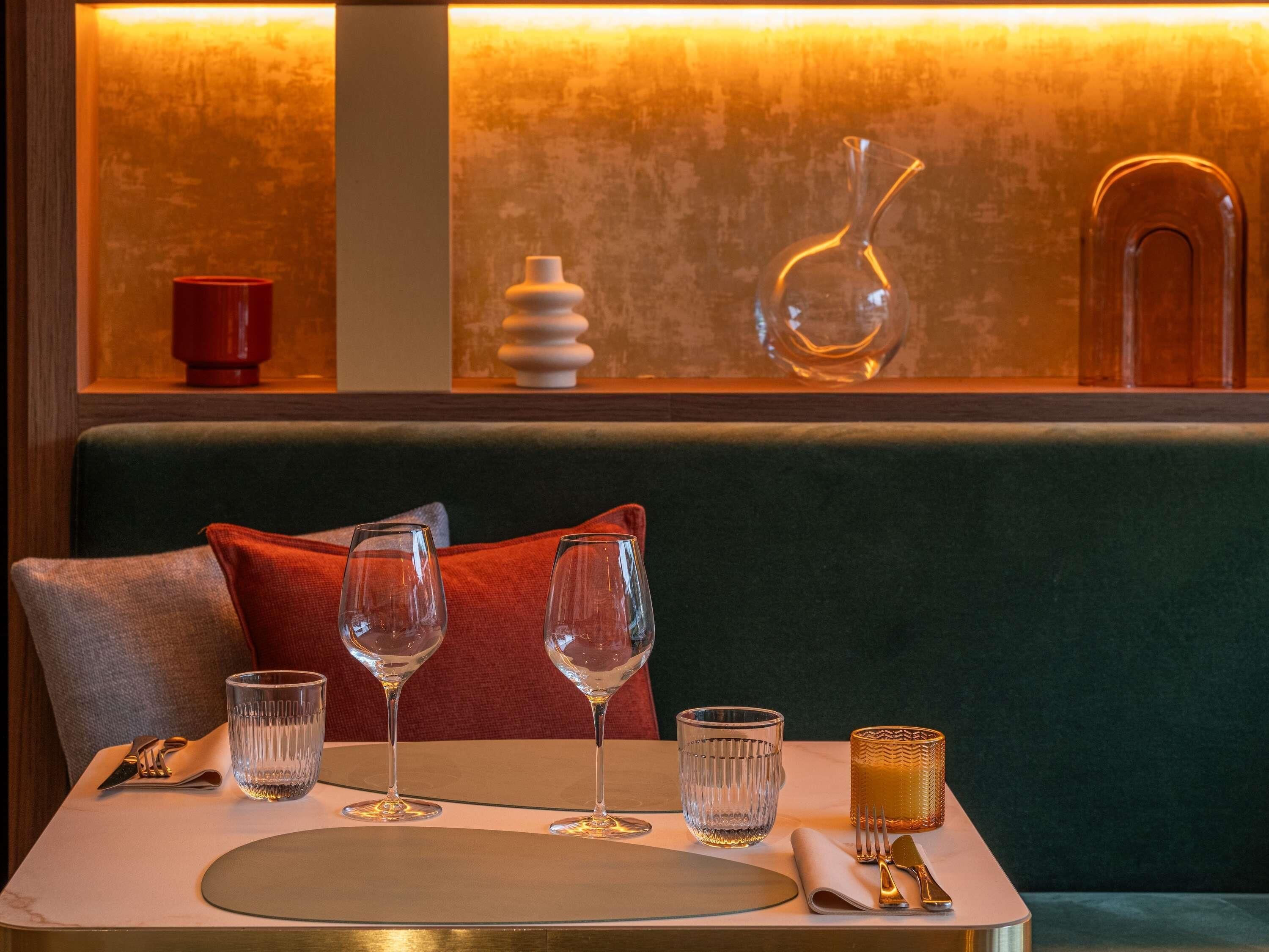A dining area with a table set for two, featuring clear glassware, a napkin, cutlery, and a decorative candle holder.