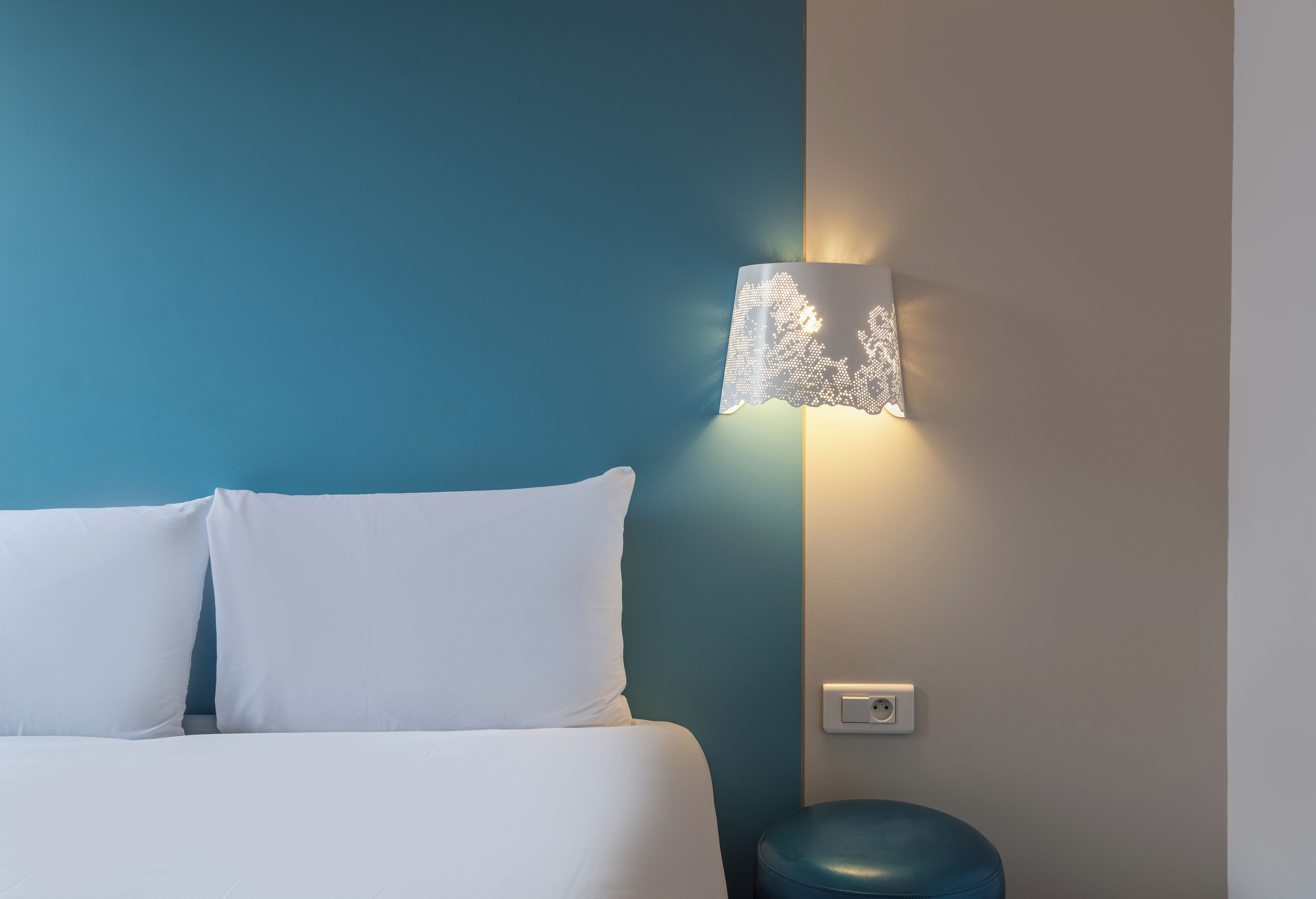 Ein Bett mit weißer Bettwäsche, eine blaue Wand und eine Wandleuchte mit Lampenschirm aus Spitze.