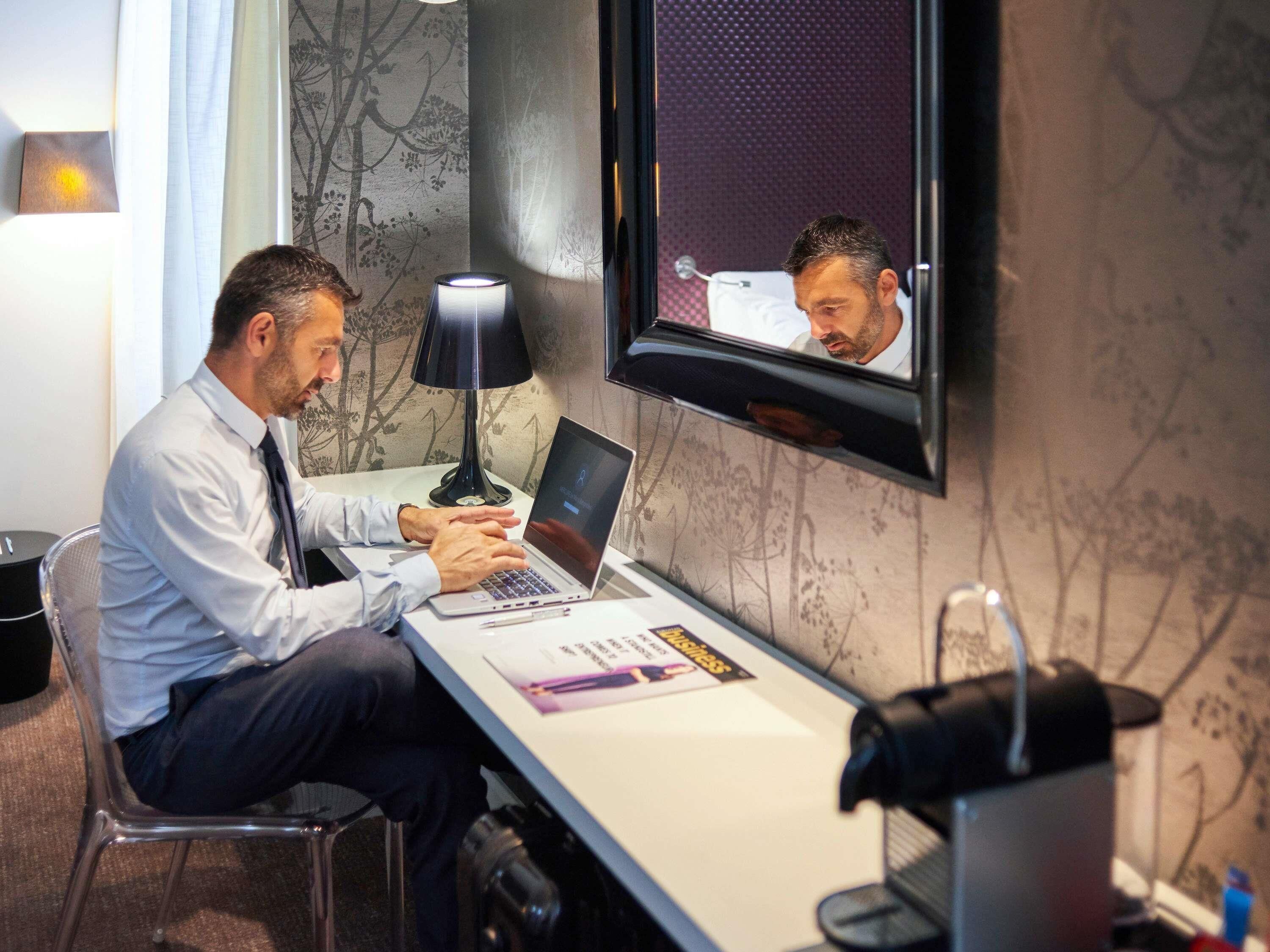 A man working at a desk with a laptop, a lamp, and a magazine.
