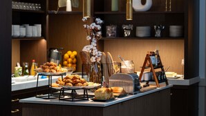 Mostrador de buffet con diversos alimentos, incluyendo pasteles y pan, en un entorno moderno de hotel.
