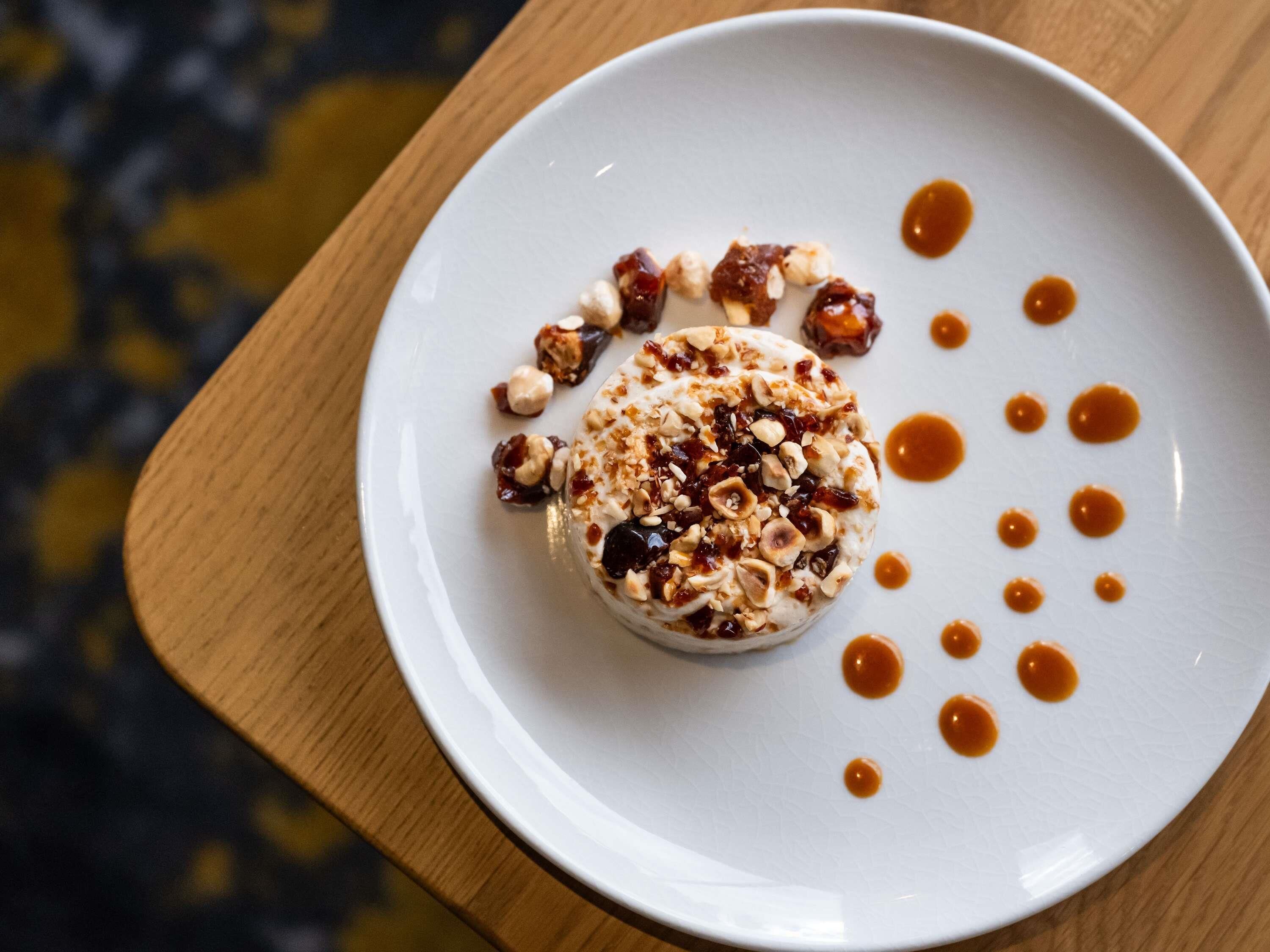 Un dessert servi dans une assiette blanche, nappé de caramel et parsemé de noix.