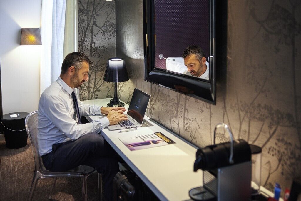 Un hombre trabajando en un escritorio con una computadora portátil, una lámpara y una revista.