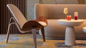 Un área de descanso moderna con un sofá, una silla de madera y una mesa redonda con dos bebidas.