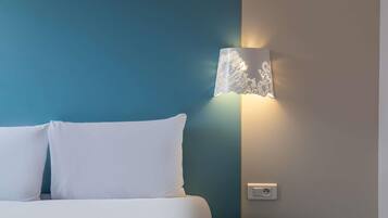 Ein Bett mit weißen Kissen, einer blauen Wand und einer Wandlampe.