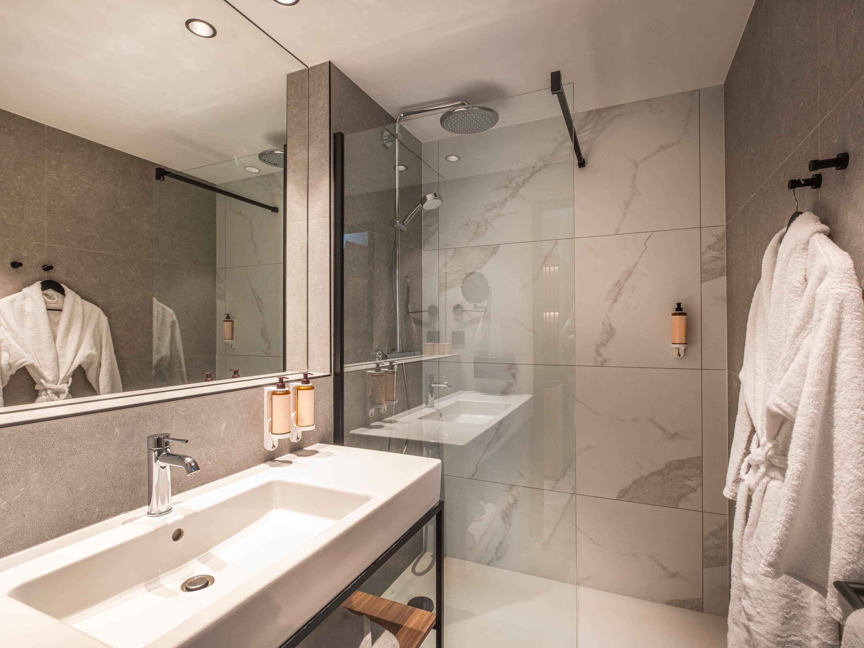 Ein modernes Badezimmer mit einer in Glas abgeschlossenen Dusche, einem großen Spiegel und zwei Waschbecken.
