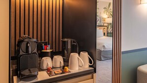 Habitación de hotel con pared de paneles de madera, una estación de café con cafetera, tazas y tetera.