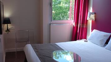 A hotel room with a bed, a chair, a table, and a window with curtains.