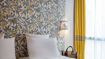 Een hotelkamer met bloemenbehang, een bed met wit beddengoed, een lamp en een geel gordijn.