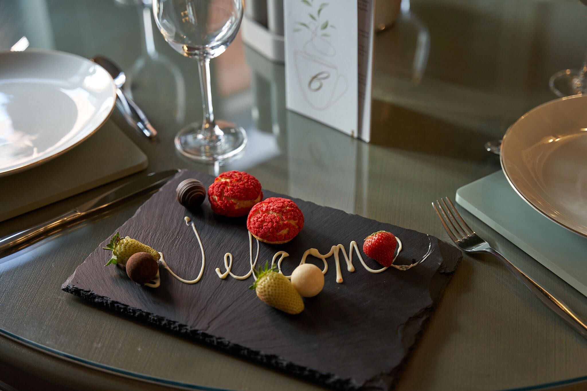 A dessert plate with 'Welcome' written in icing, accompanied by strawberries and chocolate truffles.