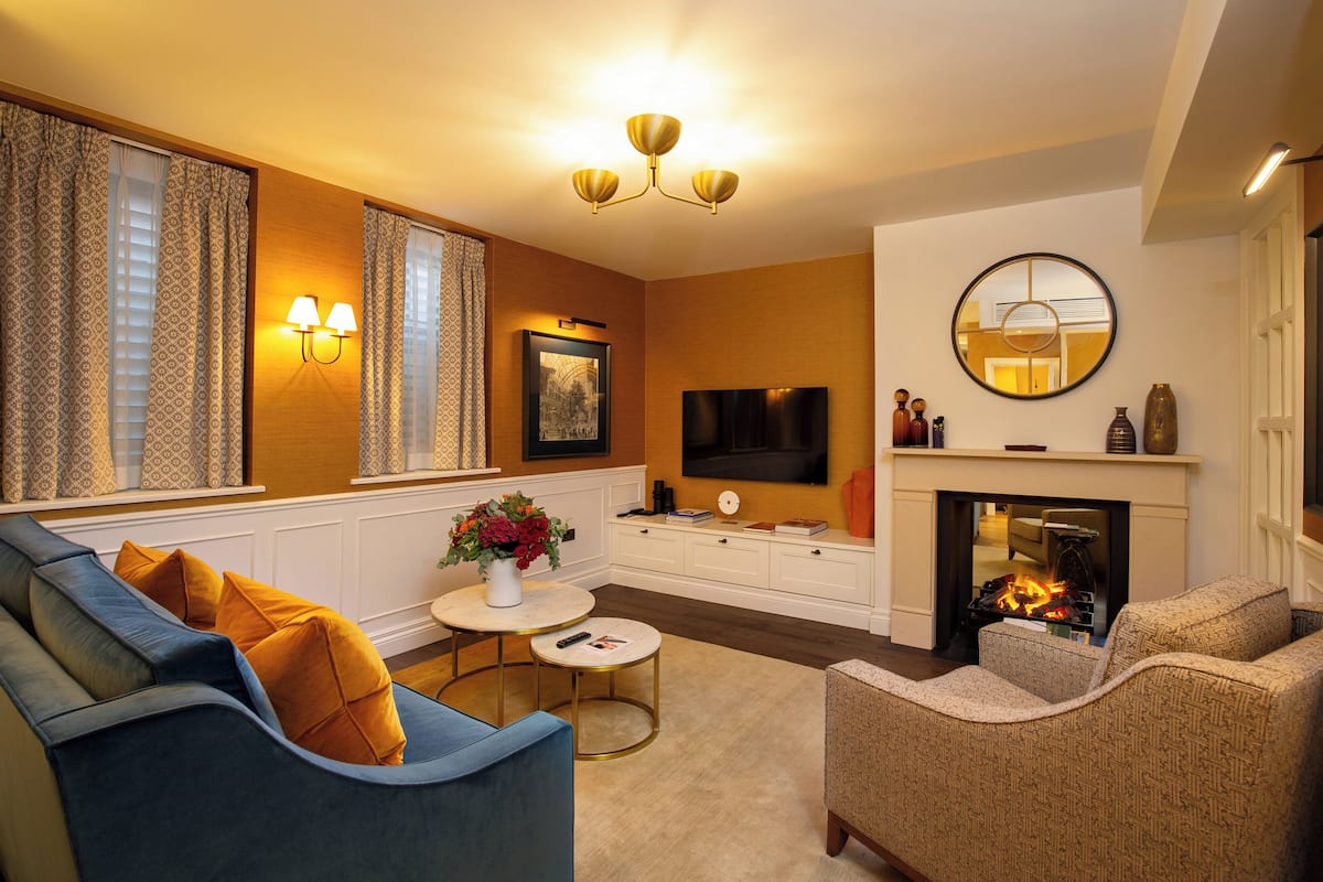 Een woonkamer met een bank, fauteuil, open haard, televisie en decoratieve accessoires.