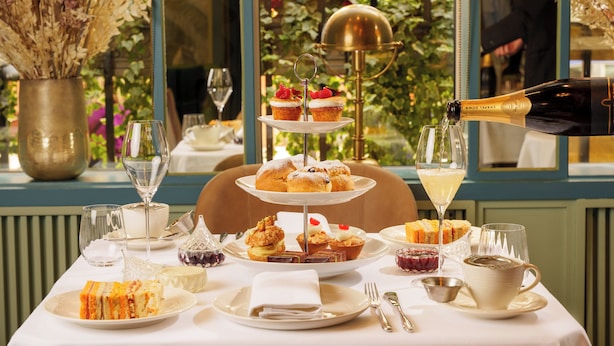 A table set for a meal with a variety of pastries and desserts, a champagne bottle being opened, and a vase of dried flowers. - The Capital Hotel, Apartments & Townhouse - Small Luxury Hotels of The World (London)