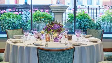 Une table dressée pour le dîner, avec vue sur un jardin grâce à de grandes fenêtres.