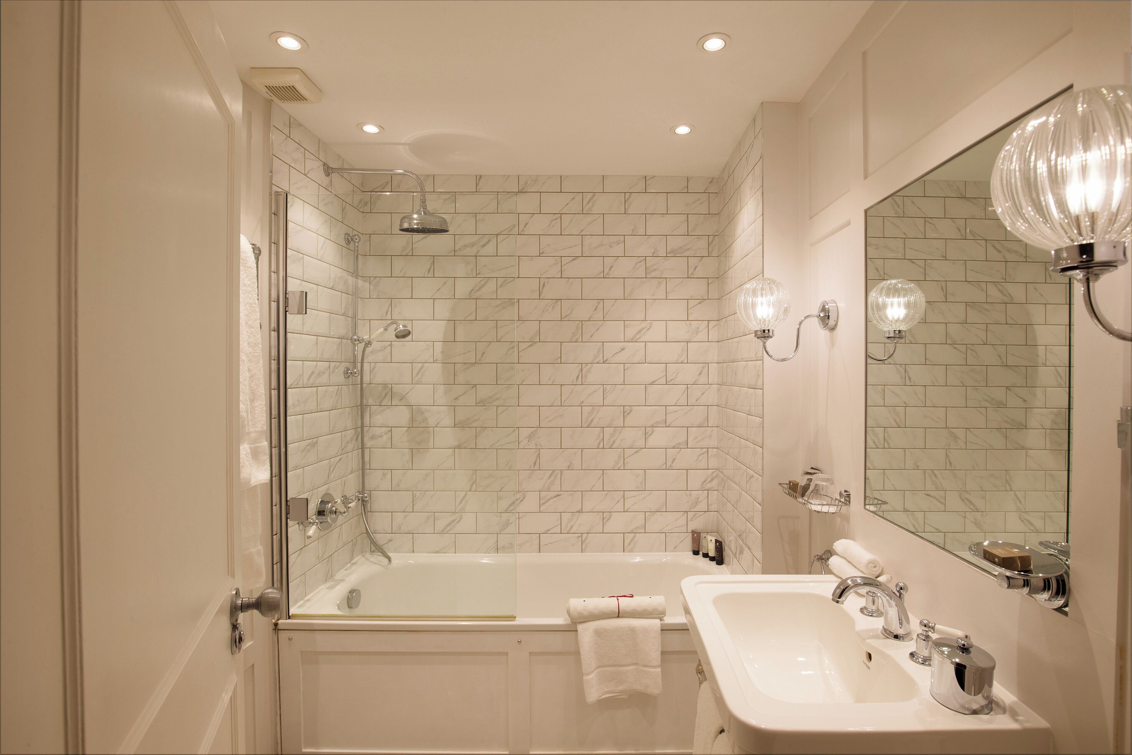 Un baño con ducha envuelta en vidrio, una bañera blanca y un lavabo con espejo.