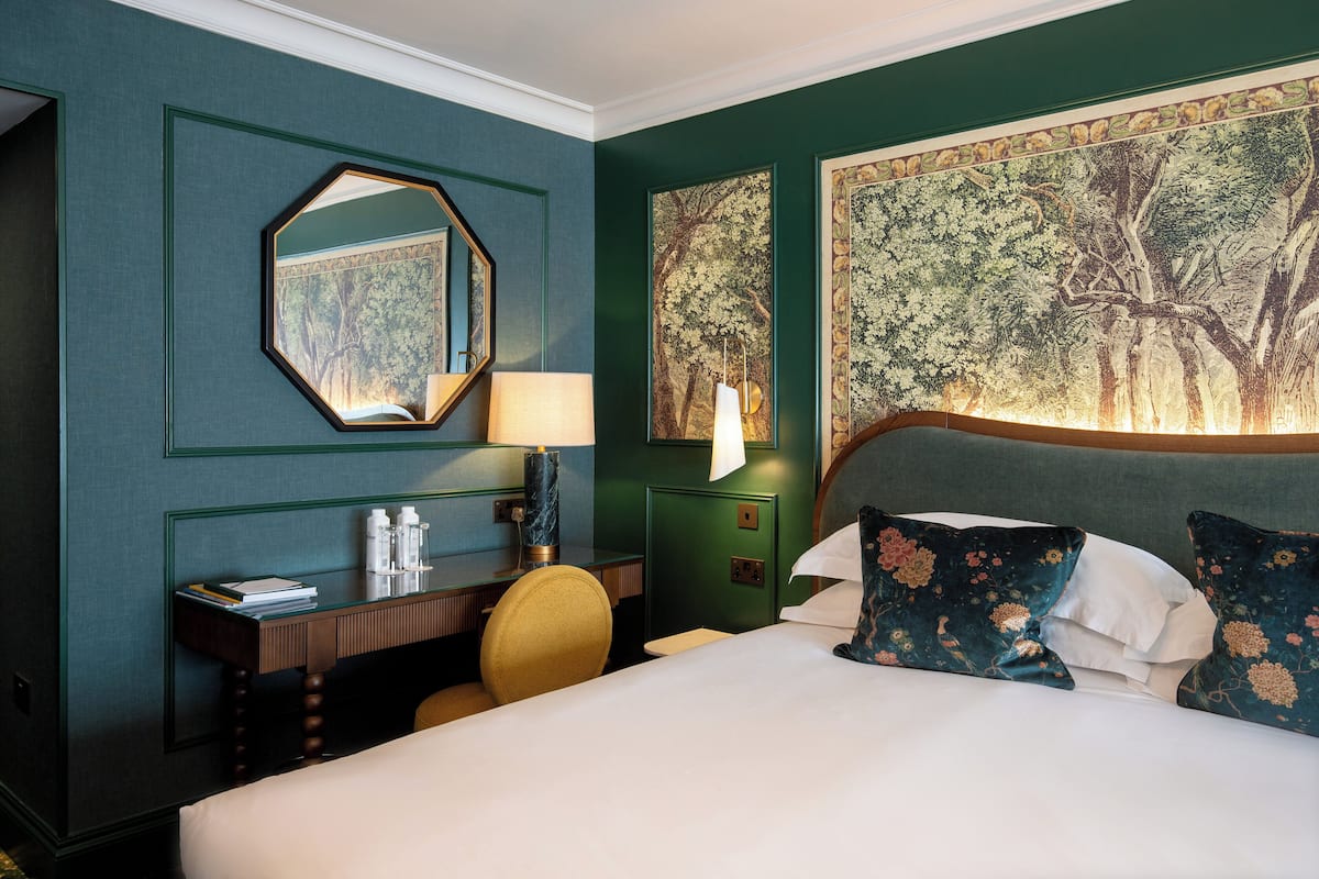 Hotelkamer met een bed, bureau, stoel, nachtkastje en een groot schilderij aan de muur.